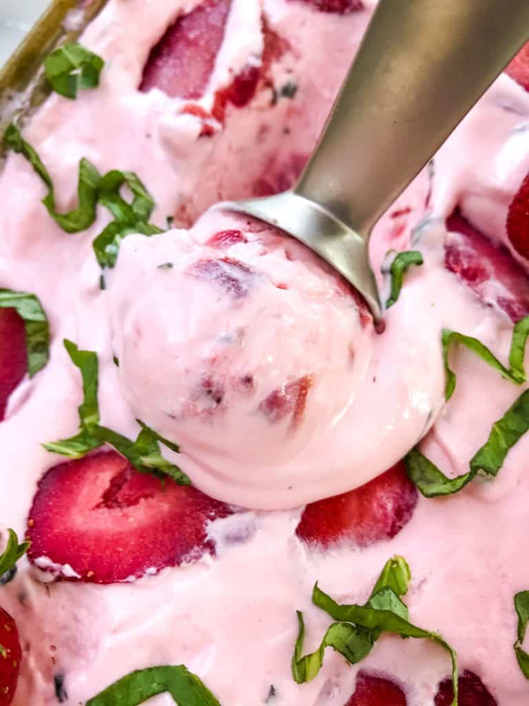 An ice cream scoop scooping out some No Churn Strawberry Basil Ice Cream