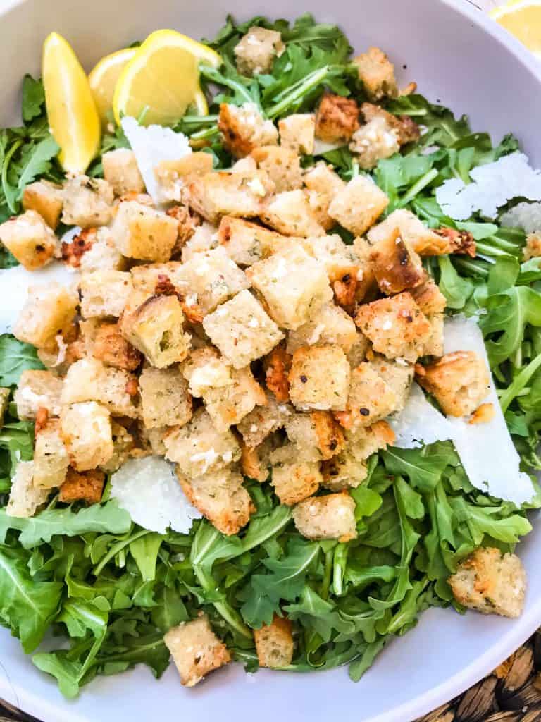 Close up of Homemade Parmesan Garlic Croutons on arugula with Parmesan shavings