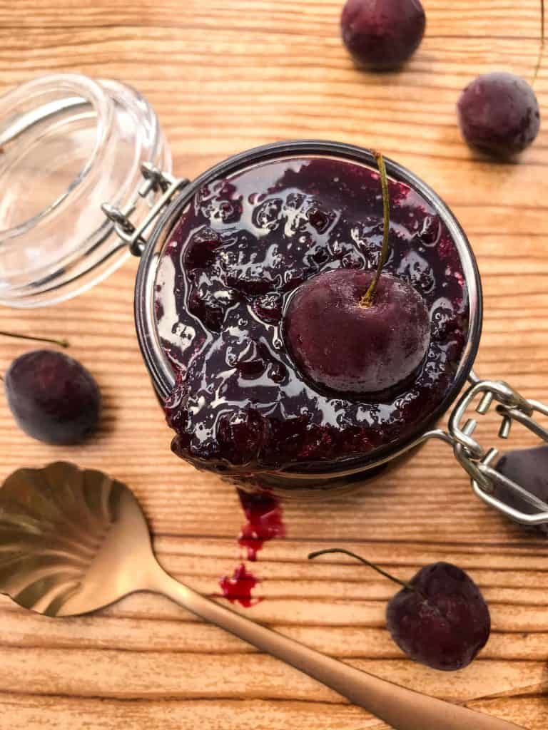 Jar of cherry jam with a copper spoon on wood