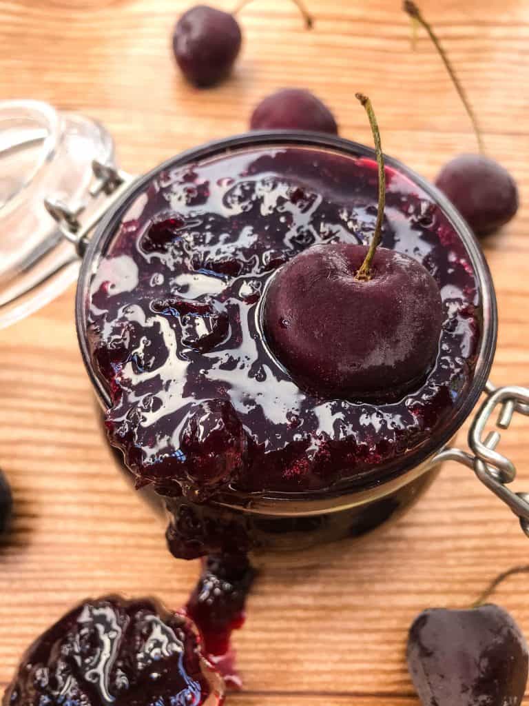 Close up of Homemade Cherry Jam in a jar with a cherry on top