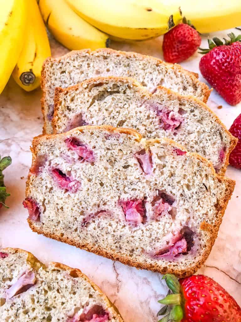 A close up of three stacked slices of Strawberry Banana Bread with bananas and strawberries around them