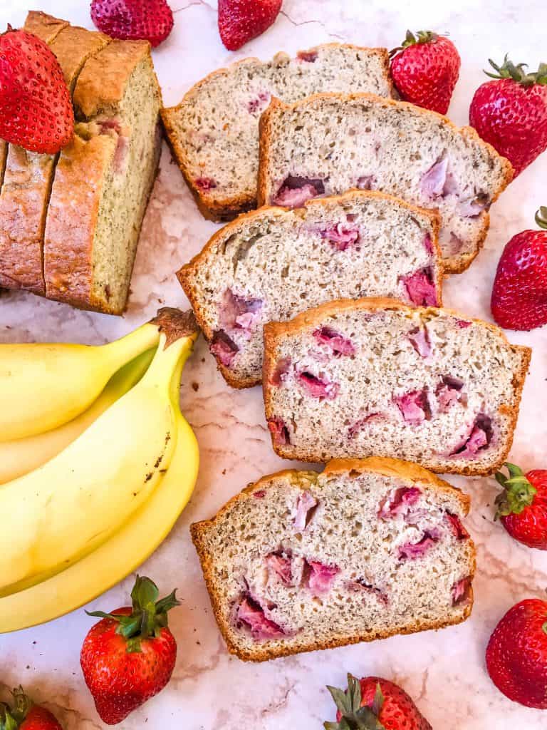 Several slices of Strawberry Banana Bread fanned out and surrounded by bananas and strawberries