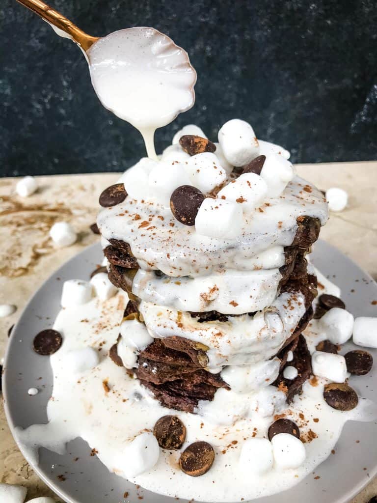 A copper spoon pouring marshmallow sauce over Hot Chocolate Pancakes