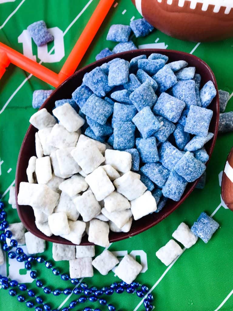 A football bowl with white puppy chow on one side and blue puppy chow on the other, on top of a green football field table cloth