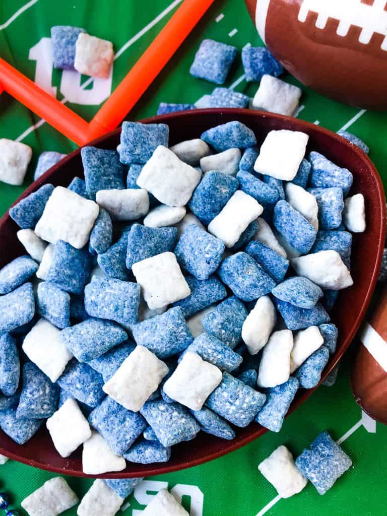 Blue and white muddy buddies mixed together in football bowl with green football field tablecloth