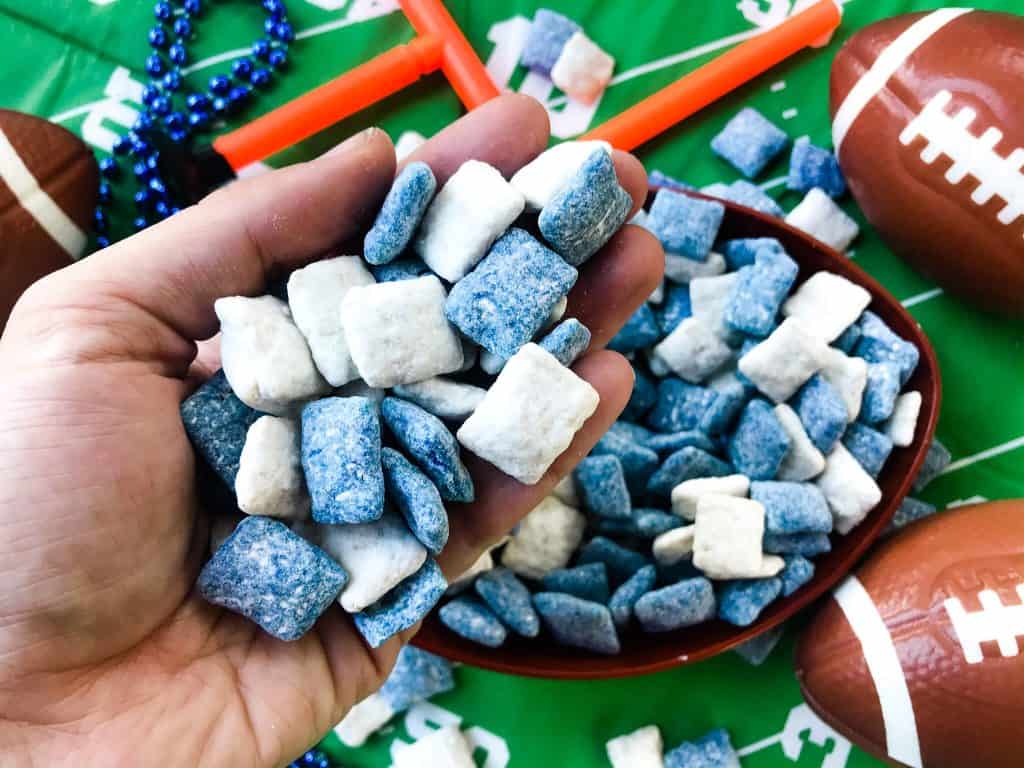 Hand holding blue and white puppy chow muddy buddies with football decor in background