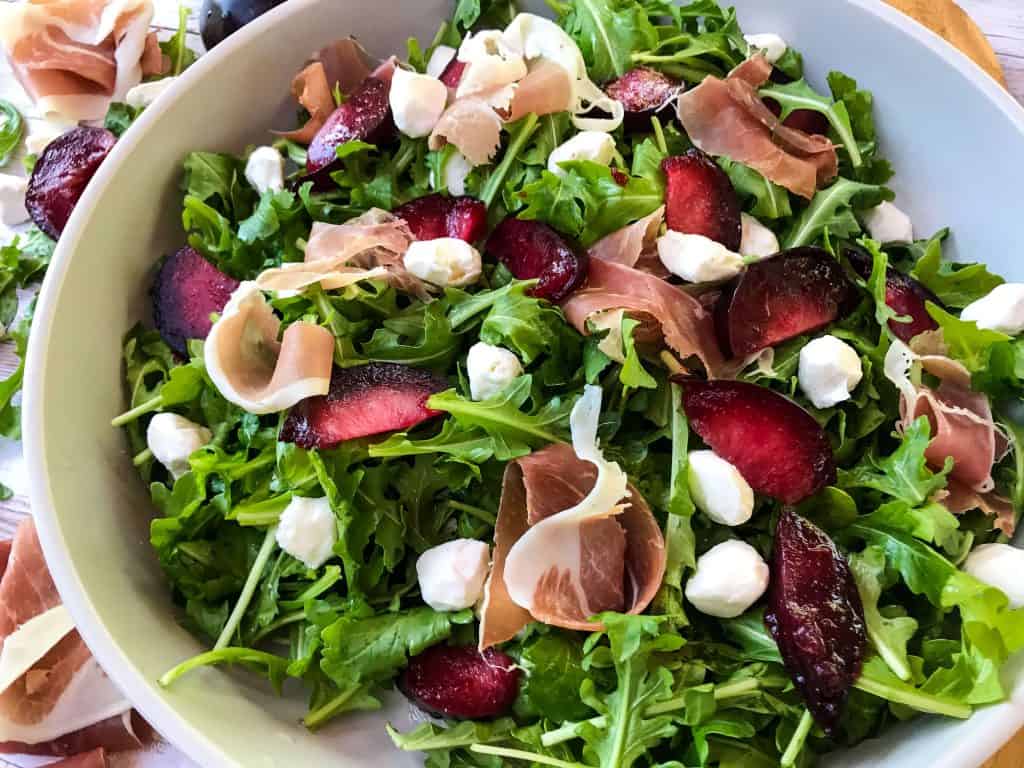 Horizontal image of Prosciutto Plum Arugula Salad with Mozzarella in a bowl