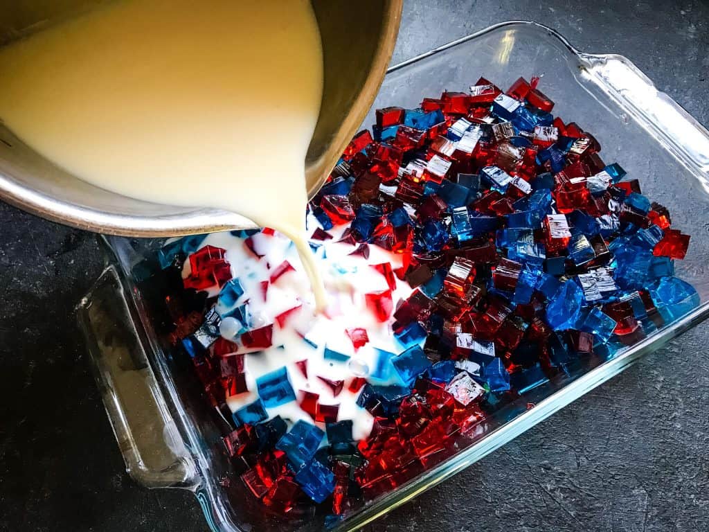 Pouring white gelatin into red and blue cubes inside a baking dish