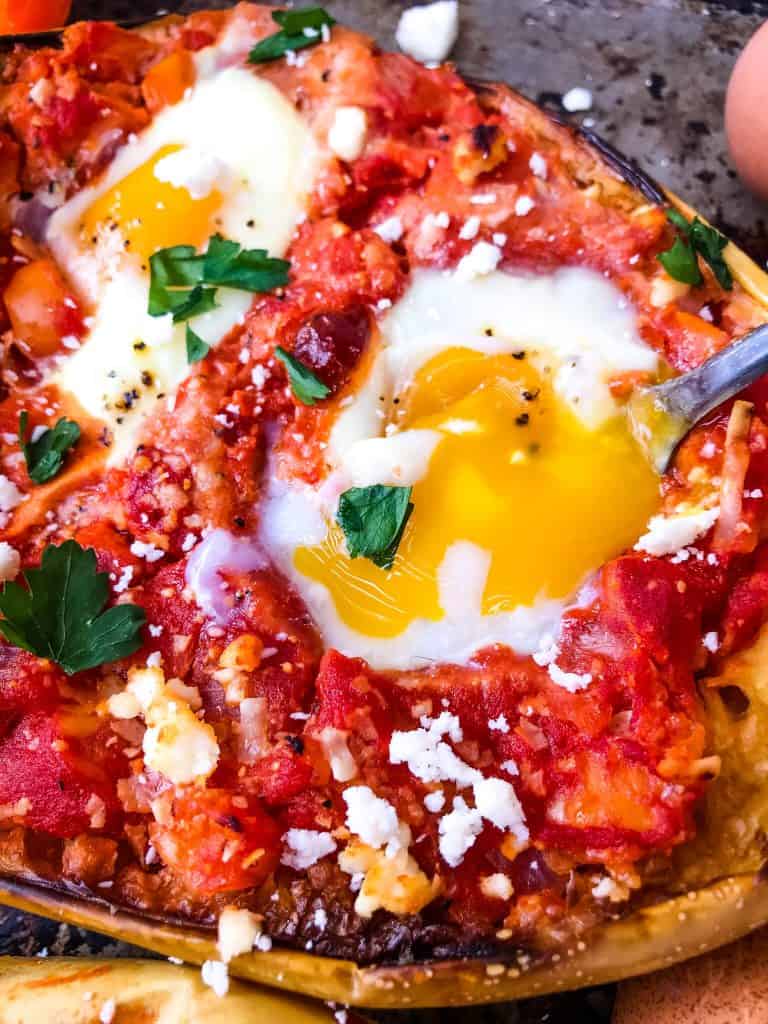 Fork digging in to a runny egg yolk cooked in a red sauce inside spaghetti squash