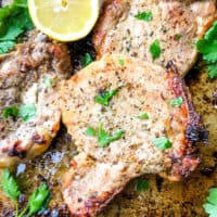 Italian Baked Pork Chops on a baking sheet with parsley and lemon