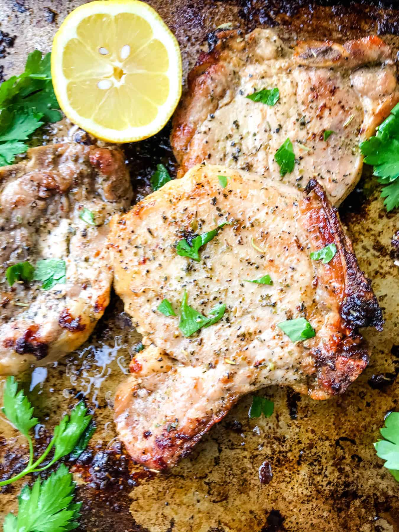 Italian Baked Pork Chops on a baking sheet with parsley and lemon