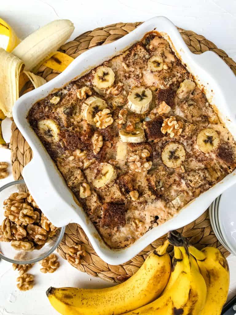 A square white dish filled with Banana Bread Pudding surrounded by bananas