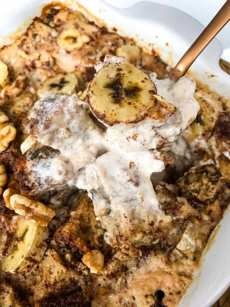 A copper spoon scooping Banana Bread Pudding out of a white dish