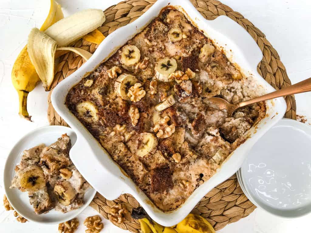 A spoon sticking out of a banana dessert on a woven mat with bananas