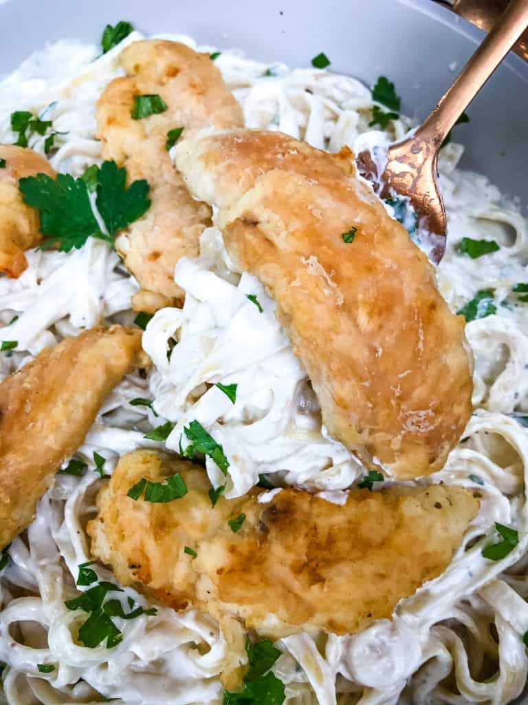 A spoon scooping some Copycat Olive Garden Chicken Alfredo out of a dish