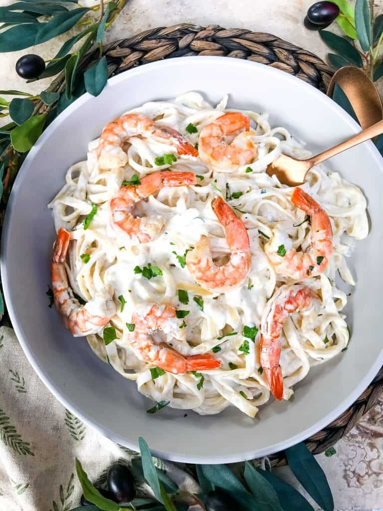 A bowl of creamy pasta with large shrimp on top