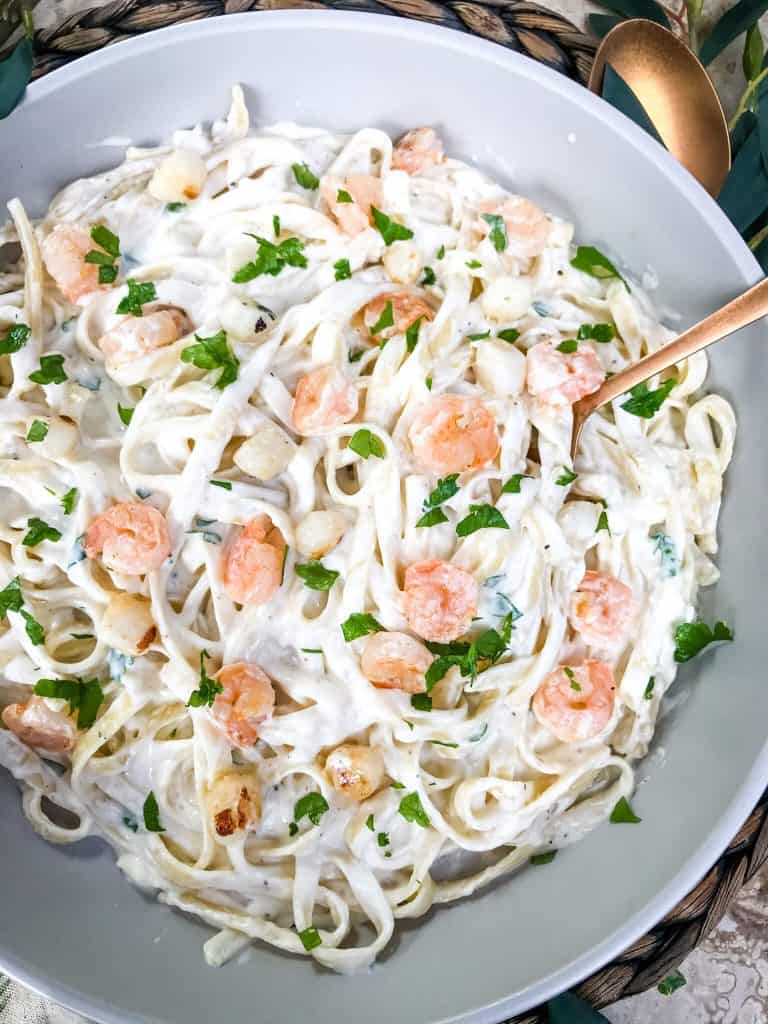 A bowl full of Copycat Olive Garden Seafood Alfredo with a spoon in it