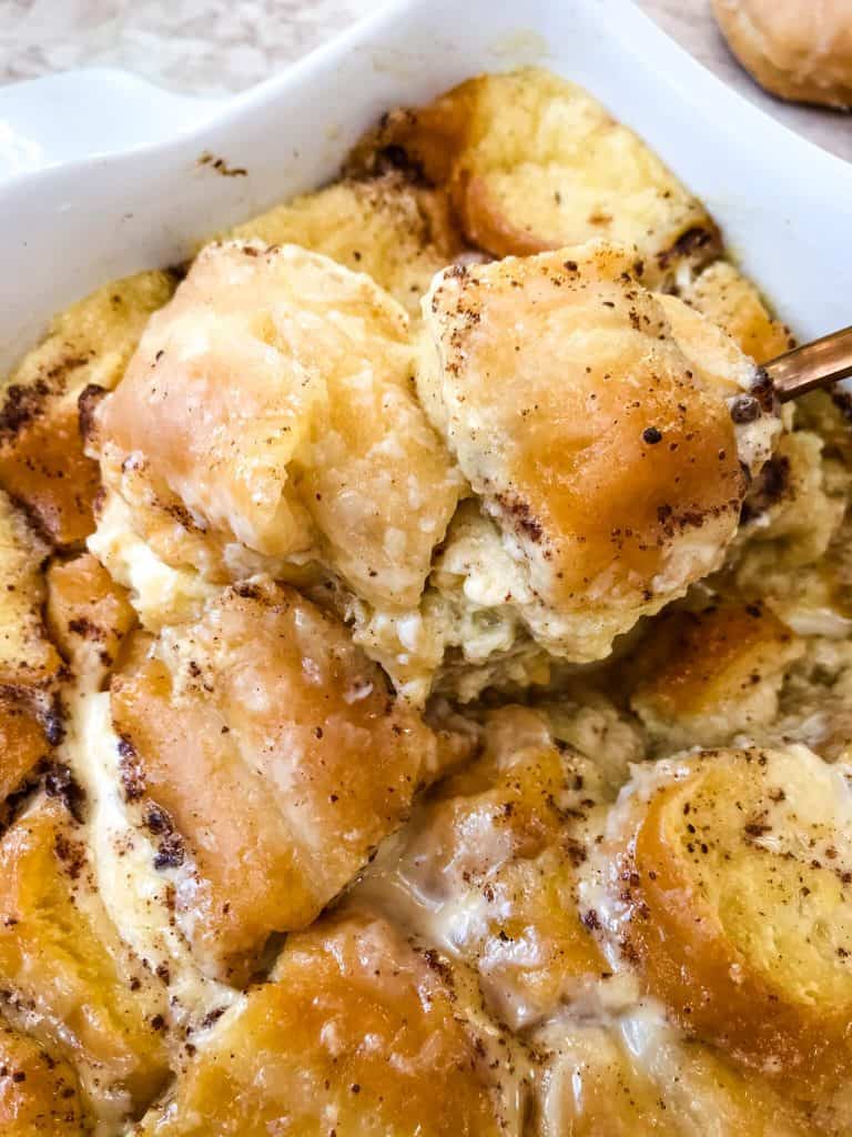 Spoon scooping Doughnut Bread Pudding out of a white dish