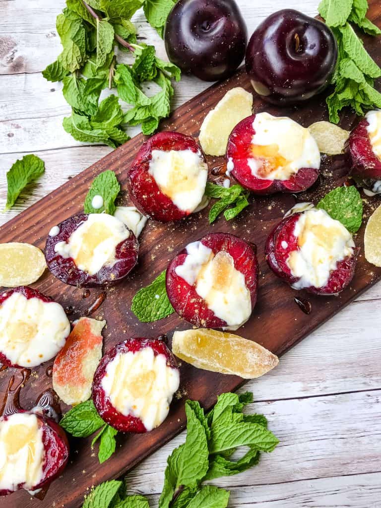 Grilled Plum Dessert with Ginger Honey Yogurt on a dark wood board surrounded by mint