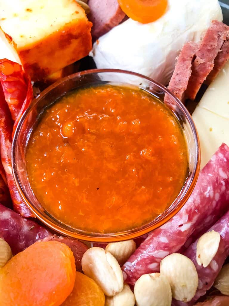 A bowl of Apricot Jam Recipe in a charcuterie board surrounded by meat and cheese
