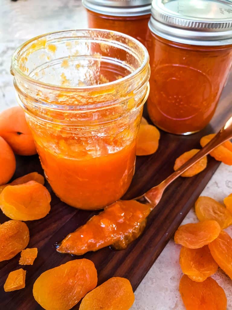 A half empty jar of Apricot Jam Recipe with jars in background and surrounded by dried apricots