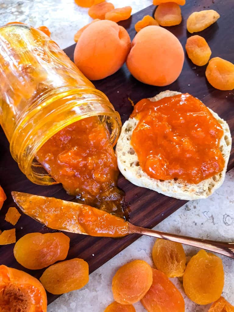 A jam jar tipped over, surrounded by apricots, and a muffin topped with jam