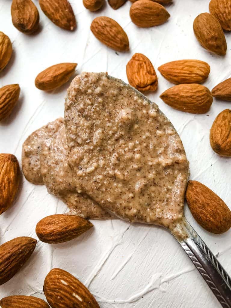 A spoon of Homemade Crunchy Almond Butter with almonds around it