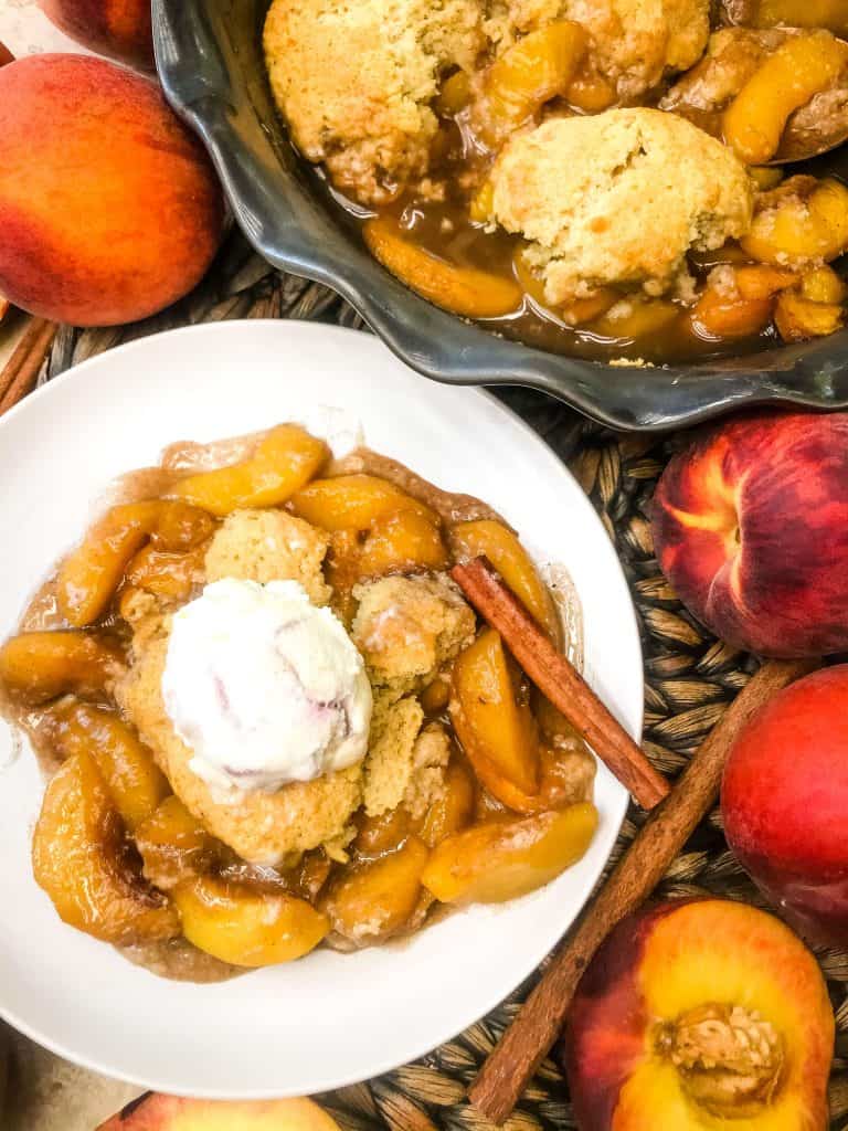 A dish of Easy Peach Cobbler with ice cream next to a cobbler dish