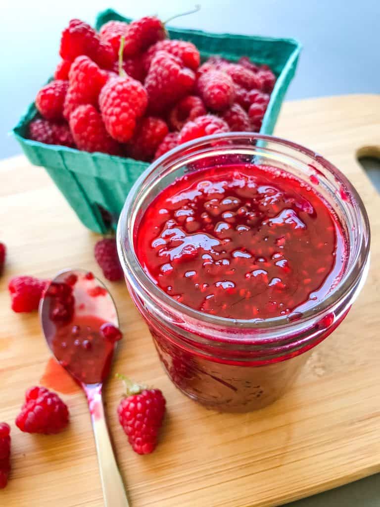 A jar of jam with raspberries behind it