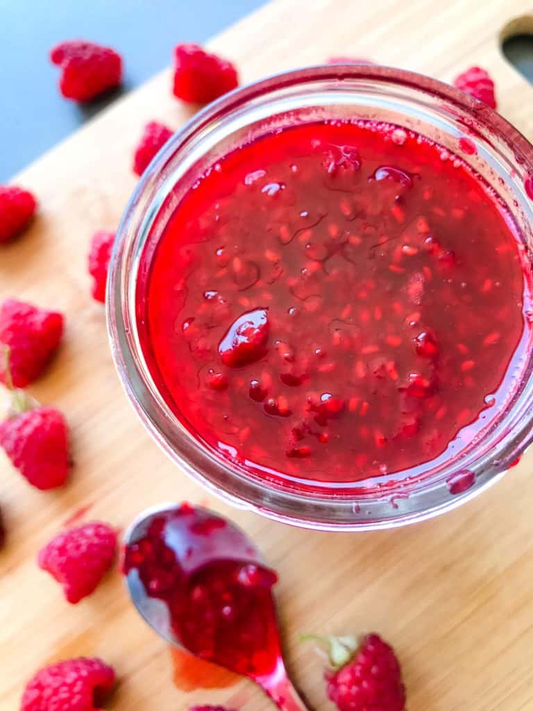 Top view of a jar of Raspberry Jam Recipe with raspberries around it