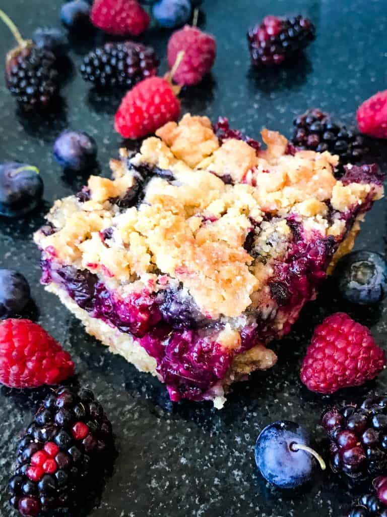 Mixed Berry Crumble Bars surrounded by berries on a black surface