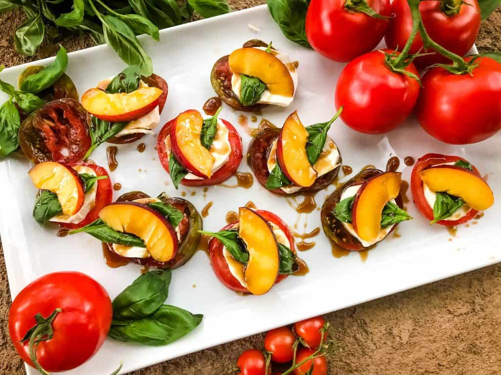 White platter of Nectarine Tomato Caprese Salad (Peach Caprese Salad) stacks with tomatoes and basil around it