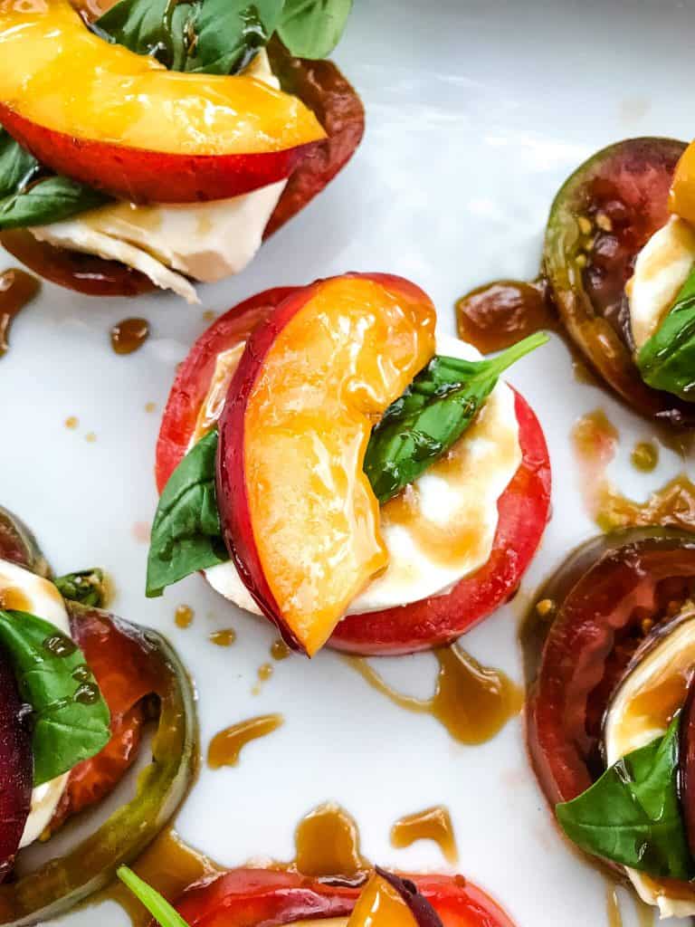 A close up of Nectarine Tomato Caprese Salad (Peach Caprese Salad) of a tomato, fresh mozzarella, basil, and nectarine slice