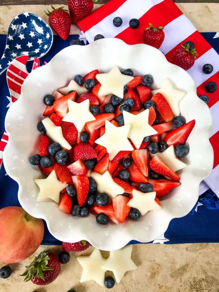 A white bowl full of strawberries, blueberries, and white star peaches