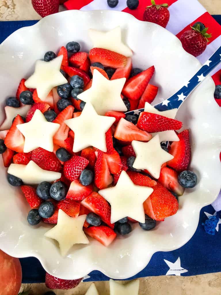 A white bowl of fruit salad with blue spoon