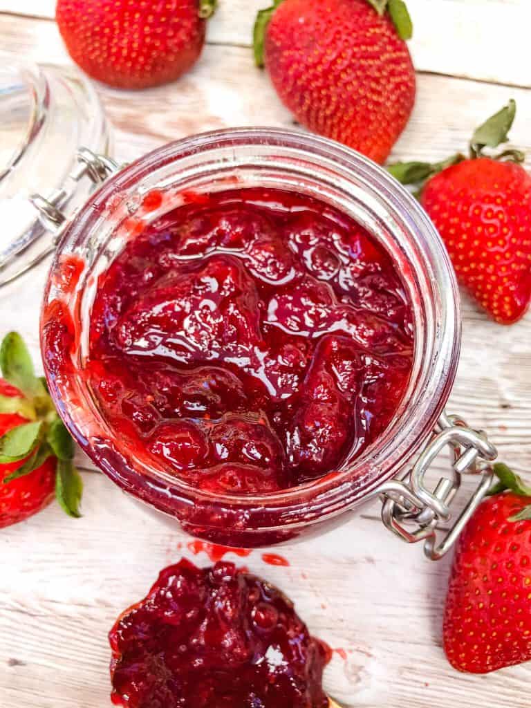 Top view of a small glass jar filled with Jam surrounded by berries on top of light wood