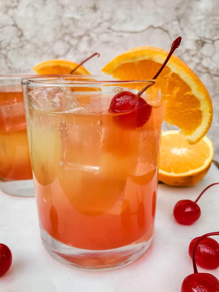 A glass of Copycat Olive Garden Venetian Sunset Champagne Cocktail with a cherry and orange slice