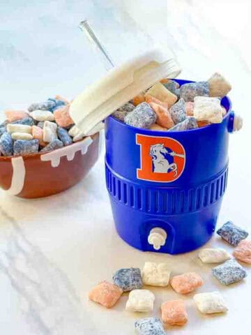 Blue, orange, and white Denver Broncos Puppy Chow in a cooler cup and on a white counter.