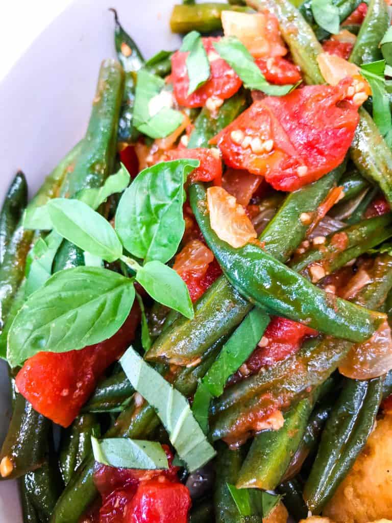A close up of Tomato Garlic Italian Green Beans with basil leaves