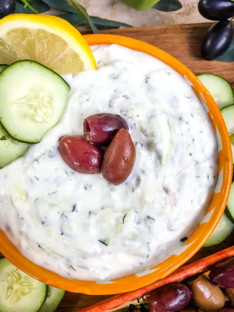 A yellow bowl of Greek Tzatziki Yogurt Sauce topped with olives