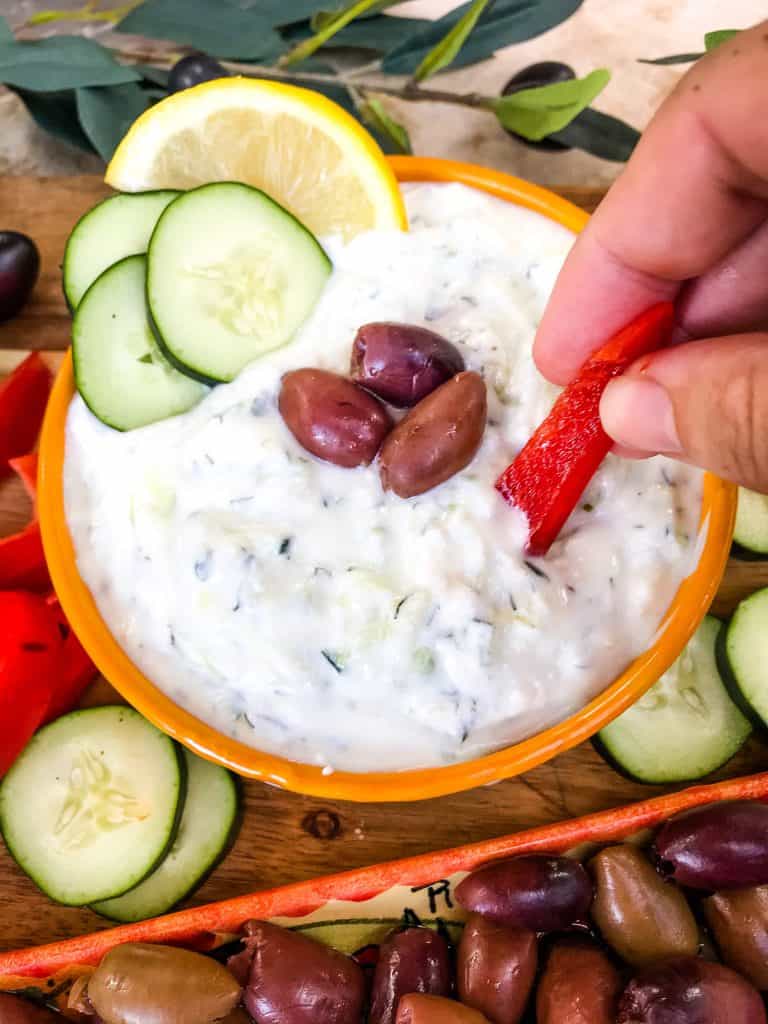 A hand dunking a pepper into a Greek sauce