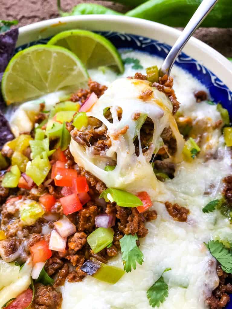 A spoon lifting melted cheese, sausage, and peppers