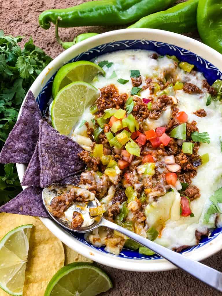 A spoon in a dish of Hatch Green Chile Chorizo Queso Fundido partially eaten