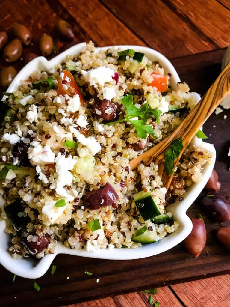 A bowl of Greek Quinoa Salad with a wood spoon
