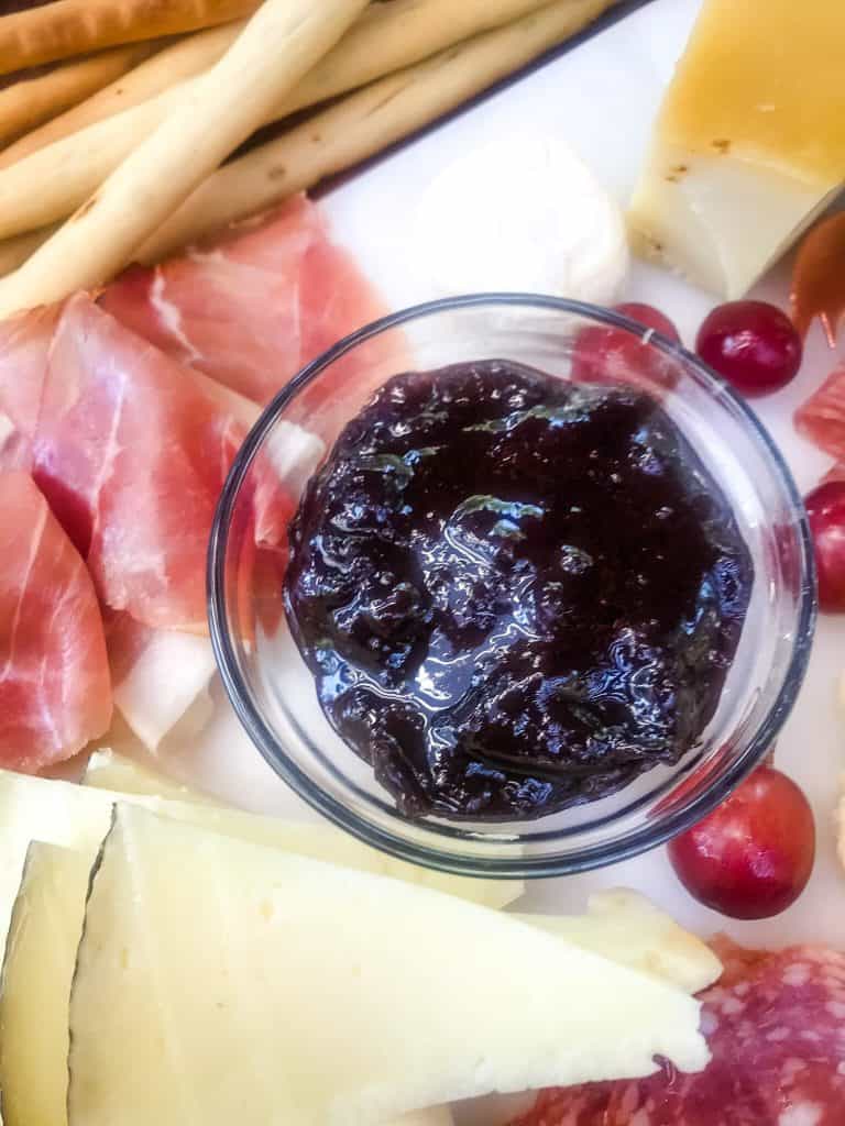 A bowl of Easy Plum Jam Recipe surrounded by cheese and meats