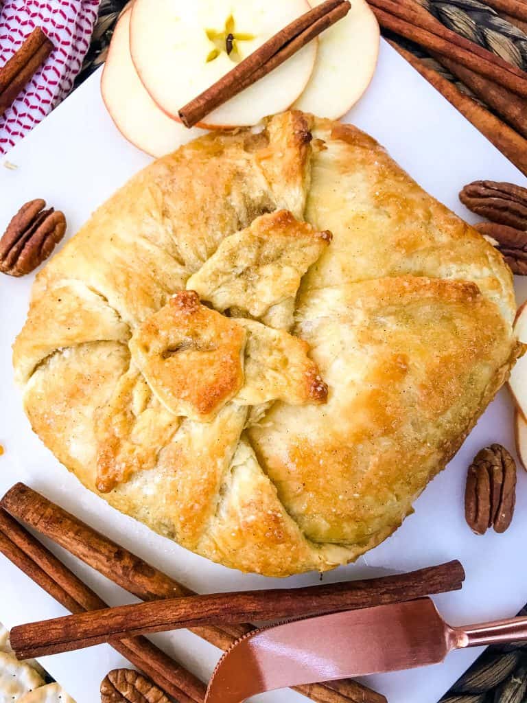 A full cheese in puff pastry surrounded by cinnamon on a white marble board
