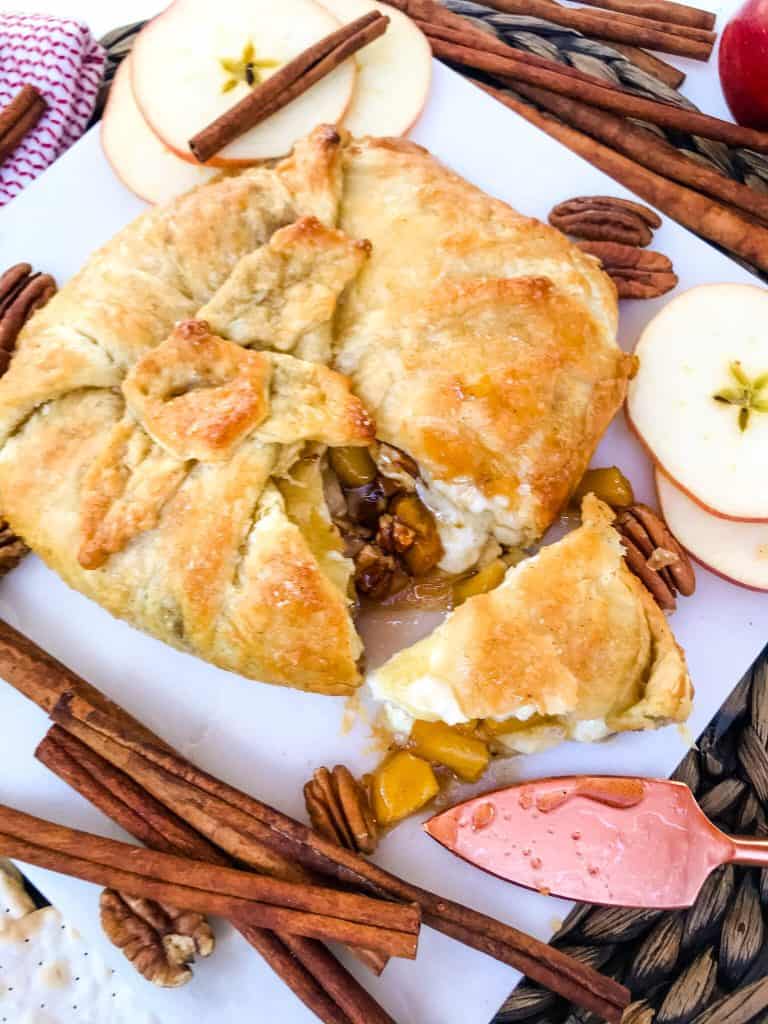 Cinnamon Apple Baked Brie in Puff Pastry on a marble board with cinnamon sticks