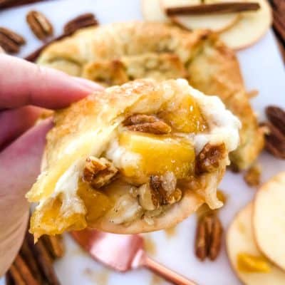 A hand holding a cracker with some Cinnamon Apple Baked Brie in Puff Pastry on it