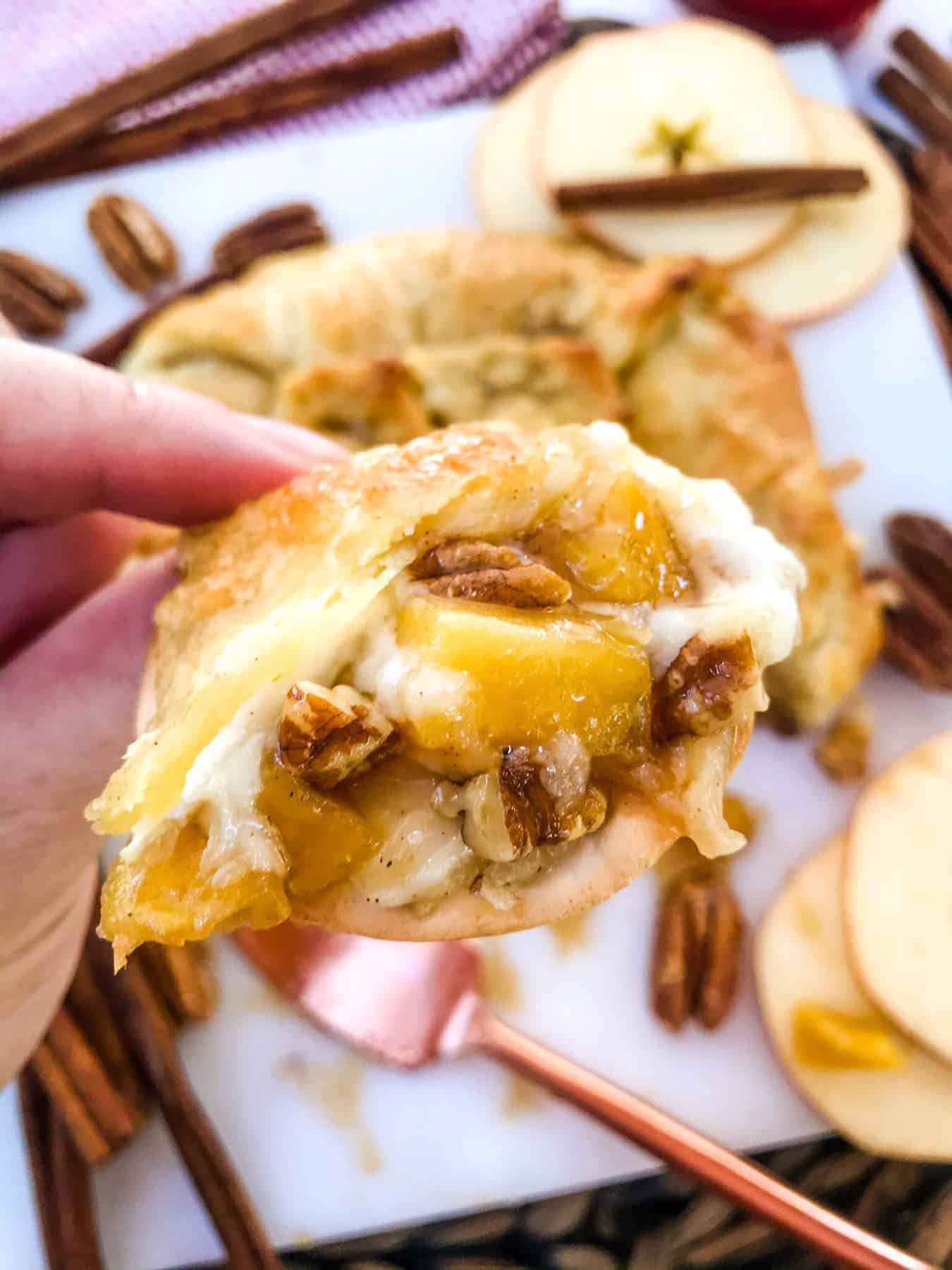 A hand holding a cracker with some Cinnamon Apple Baked Brie in Puff Pastry on it