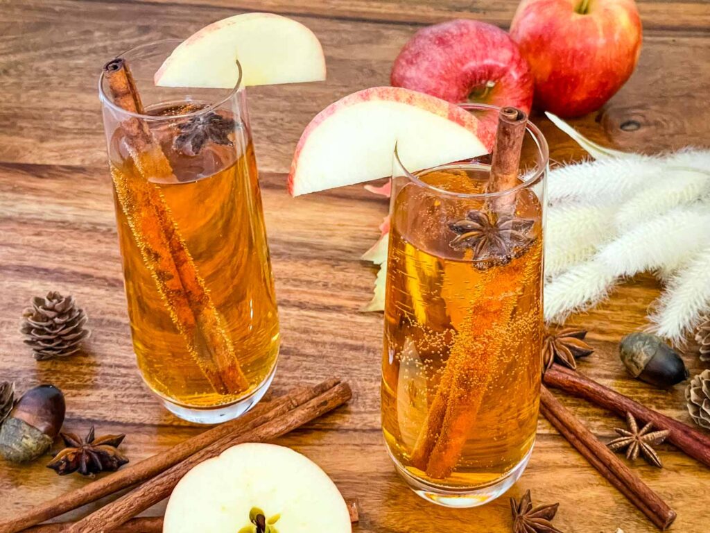 Two flutes of Cinnamon Apple Cider Mimosa on a wood table.